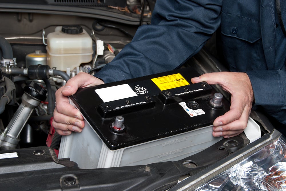 Automotive technician installing a new car battery under the hood