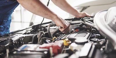 Automotive technician performing engine maintenance under a vehicle hood